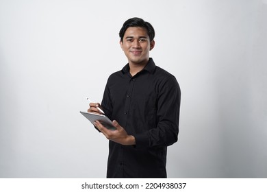 Potrait Of Asian Guy Millenial. Work Online, Freelance, Teacher And Blogger. Smiling Cute Young Male In Casual Black Looks In Digital Tablet And Surfing On Internet, Isolated On White Background, Stud