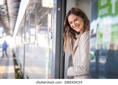 Potrait of beautiful traveler woman getting off the train smiling - Young business woman peeking out of a train door looking someone 