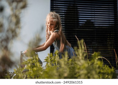 Potrait of little girl taking care of flowers in the garden, holding watering can and watering raised garden bed. - Powered by Shutterstock