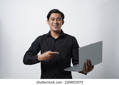 Potrait Of Smiling Asian Young Asian Man In Black Casual Shirt Pointing Finger On Computer Over White Background.