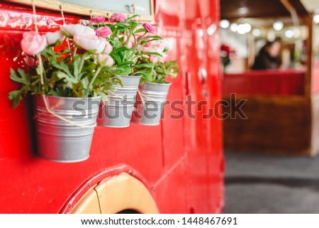 Pots with decoration plants hanging from a red bus in a vintage car exhibition.