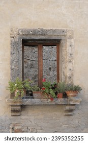 Potted, flowering plants are arranged on a stone shelf outside a window of an old, stone builiding in Tuscany, Italy