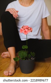 Potted Plant Geranium With Blossom, Books, Woman Sitting On The Floor. Greenery, Flower. Diseases. Aging, Wilting. Houseplant Care. Gardening, Floristry As A Hobby. Urban Jungle. Artisanal. Romance.