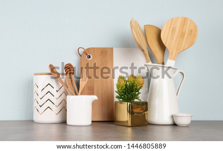Potted plant and set of kitchenware on grey table near light wall. Modern interior design