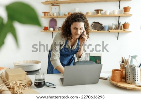 Potter entrepreneur using laptop in workshop, smiling