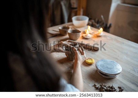 Potter hands shape patterned clay cup on wooden table in workshop. Craftsmanship, ceramic design, pottery class, handmade crockery, creative occupation, craft and master class, do it yourself