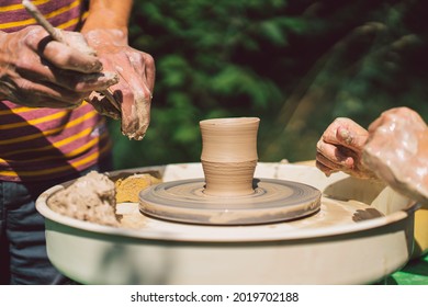 Potter making a clay object on pottery wheel in outdoors. Craftsman moulding clay with hands on pottery wheel