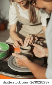 Potter teaches apprentice how to create clay pot on pottery wheel, passing down knowledge and skills