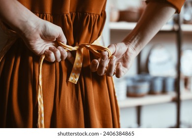 Potter woman getting ready for work by putting on apron in workshop Hands of woman close-up tying apron, back view. - Powered by Shutterstock