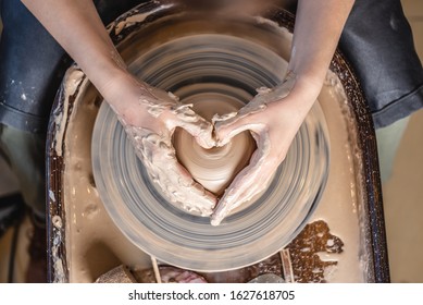 A Potter works with clay on a Potter's wheel in the workshop. Women's hands show a heart sign. The concept of love for pottery art and creativity. Top view - Shutterstock ID 1627618705