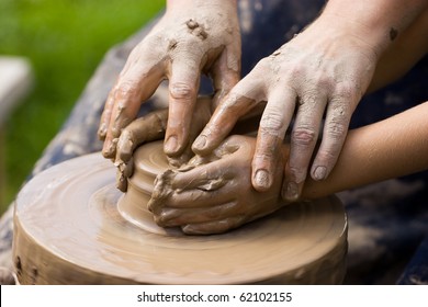 A potters hands guiding a child hands to help him to work with the ceramic wheel - Powered by Shutterstock