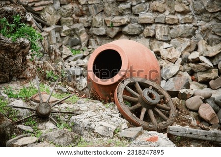 pottery jug and old wooden wheel near stone wall