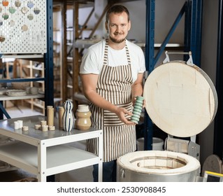 In pottery workshop, guy master takes finished pottery out of oven. Final stage of manufacture of clay products, firing in oven