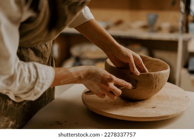 In the pottery workshop the master processes the product with loop for clay sculpts clay dishes on table - Powered by Shutterstock