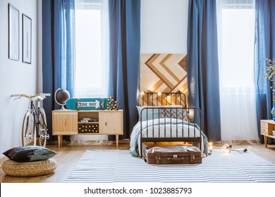 Pouf And Bike In Cozy Teenager's Bedroom Interior With Blue Curtains And Wooden Cupboard Next To Bed