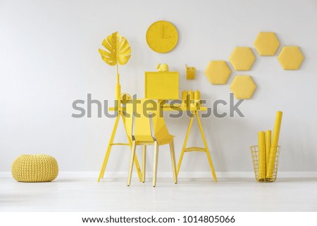 Pouf next to chair at desk with monstera leaf against white wall with honeycombs in yellow room interior