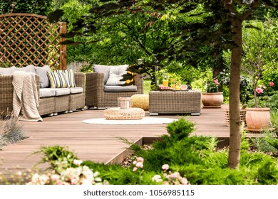 Pouf On White Round Rug Near Garden Furniture With Blanket And Pillows On Wooden Patio