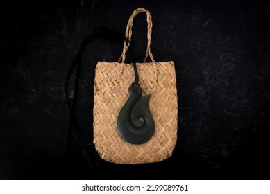 Pounamu Fish Hook Necklace On Weaved Bag On Dark Background. Aotearoa, New Zealand, Maori.