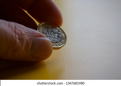 Pound Coin Held By Fingertips On Yellow Background