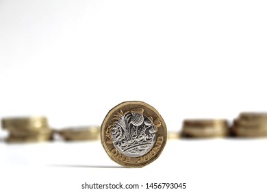 Pound coin standing up in focus with other pound coins out of focus behind it on a white background