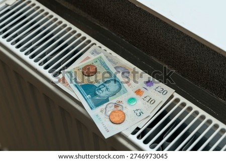 Pound sterling notes and coins are placed on a radiator in a room. The sunlight shines on the currency, highlighting the different denominations and colors of the money.