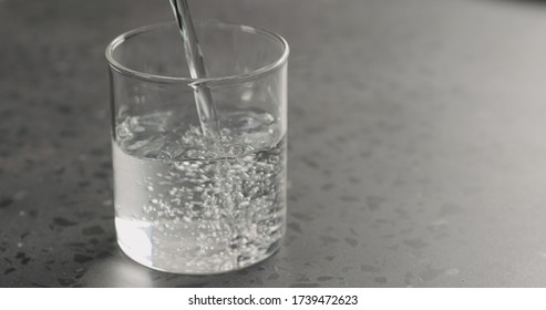 Pour Clean Fresh Water In Beaker Glass On Concrete Countertop