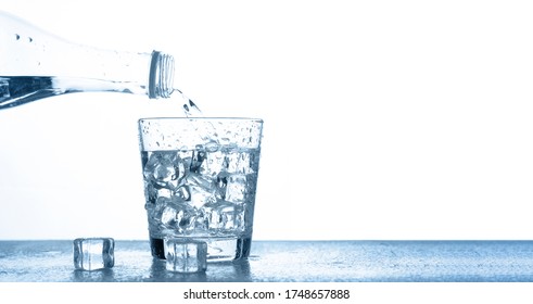 Pour Drinking Water Into A Clear Glass With Ice On The Table On A White Background With Copy Space.