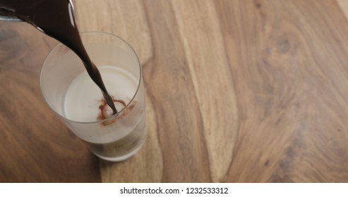 Pour hot cocoa in glass with oat milk on wood background with copy space