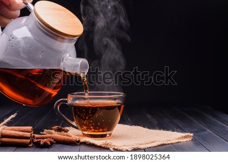 Pour the hot tea into the teacup. A teacup placed on an old wooden table In a black background, there was soft sunlight shining into a warm atmosphere.