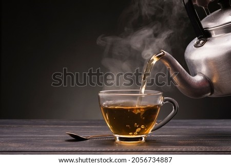 Pour hot tea into a teacup placed on a wooden table with, dark black background