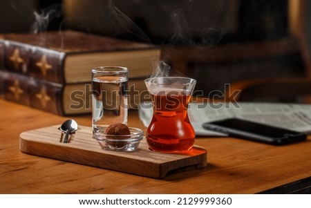 Pour the hot tea into the teacup. A teacup placed on an old wooden table, with books