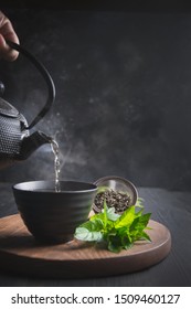 Pour hot tea with steam into cup on black table. Chinese tea. Asian still life.