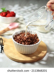 POur Milk To The Bowl With Chocolate Flavoured Rice Crispy, Breakfast Cereal In A White Bowl 