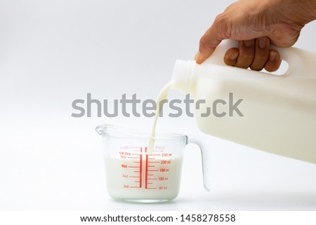 pour milk in glass measuring cup on white background