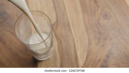 pour oat milk in glass on wood background with copy space