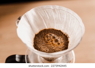 Pour over filter with ground coffee in the funnel in focus. Drip filter coffee brewing. Pour over alternative method of pouring water over roasted and ground coffee beans contained in filter - Shutterstock ID 2273942445