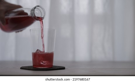 Pour Red Berry Sparkling Drink Into Tumbler Glass With Ice On White Oak Table, Wide Photo