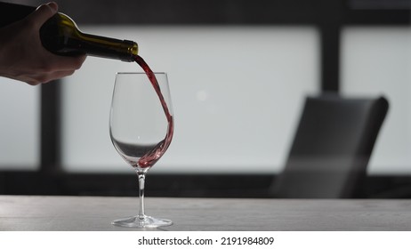 Pour Red Wine Into Wineglass On White Oak Table With Copy Space