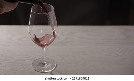 Pour Red Wine Into Wineglass On White Oak Table With Copy Space