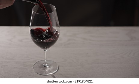 Pour Red Wine Into Wineglass On White Oak Table With Copy Space