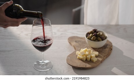 Pour Red Wine In Wineglass With Antipasti On White Oak Table