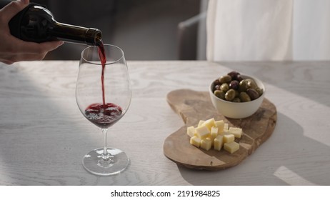 Pour Red Wine In Wineglass With Antipasti On White Oak Table