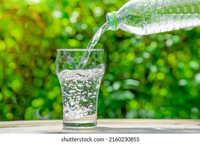 Pour water from a plastic bottle into a glass. The background of the plants in the garden. soft focus. - Powered by Shutterstock