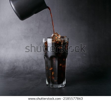 Poured coffee of ice americano coffee into a transparent glass on  black background studio photo