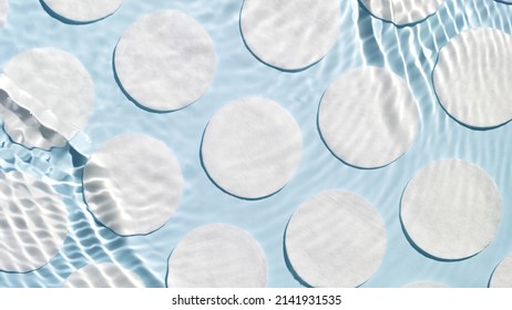 Poured water splashing and making ripples over cotton pads arranged in rows on blue background | Skin care product background, cleansing lotion commercial - Shutterstock ID 2141931535
