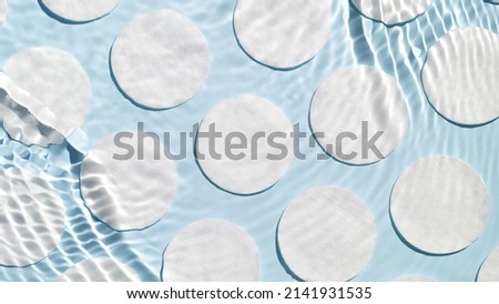 Poured water splashing and making ripples over cotton pads arranged in rows on blue background | Skin care product background, cleansing lotion commercial