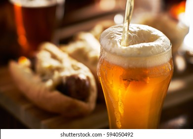 Pouring Amber Beer Into Mug With Bratwursts In Background