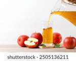 Pouring apple juice into the glass with apples fruit on wooden table.