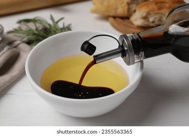 Pouring balsamic vinegar into bowl with oil on white table, closeup - Powered by Shutterstock