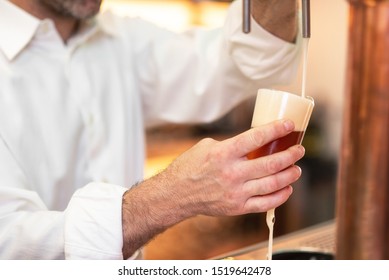 Pouring beer for client. Bartender pouring beer while standing at the bar counter .
